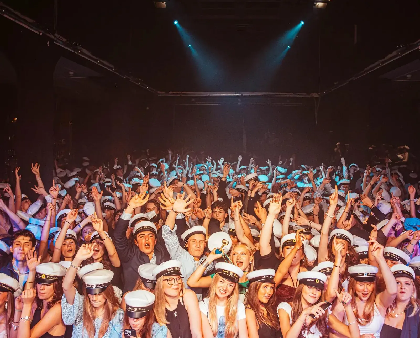Fullt dansgolv med elever i studentmössor och armarna i luften under en skolfest.