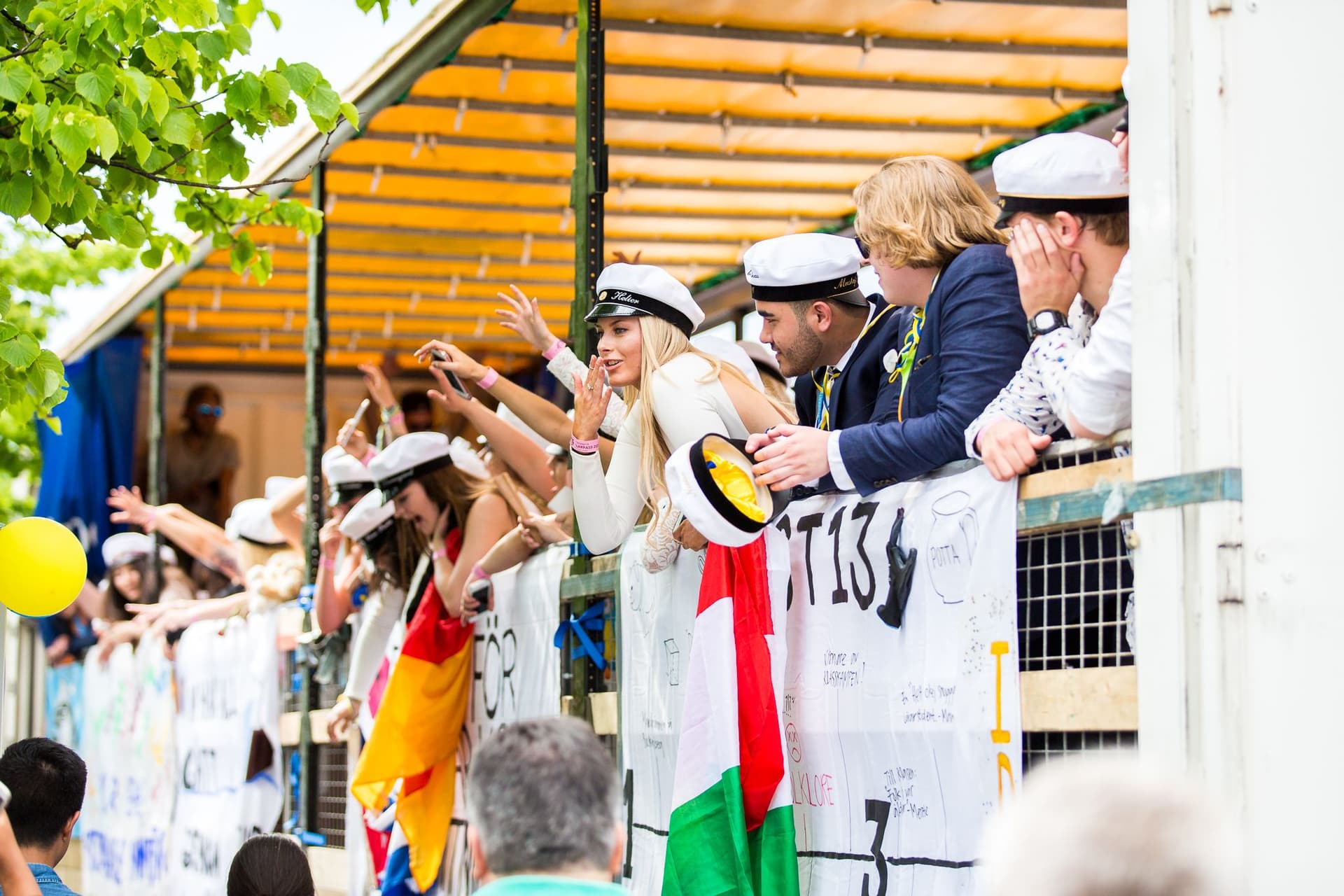 Studenter i vita studentmössor firar med flaggor och banderoller på studentdagen.